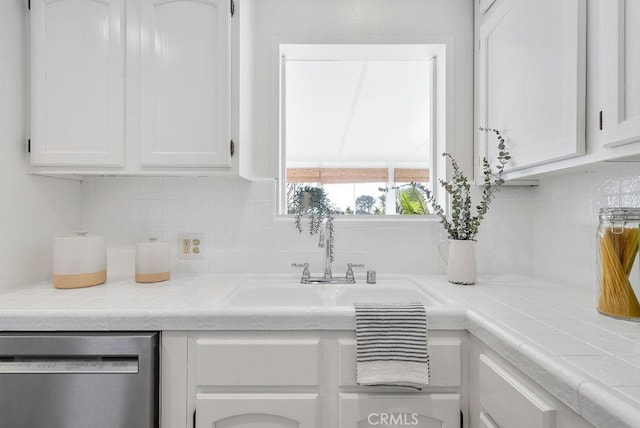 kitchen featuring dishwasher, tile countertops, backsplash, white cabinetry, and a sink