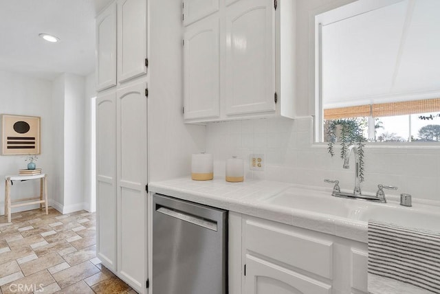 kitchen with tasteful backsplash, white cabinets, stone finish floor, stainless steel dishwasher, and recessed lighting