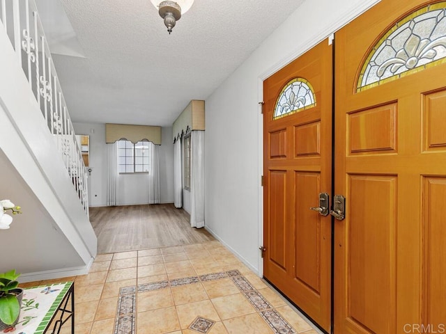 foyer entrance with stairs, light tile patterned floors, baseboards, and a textured ceiling