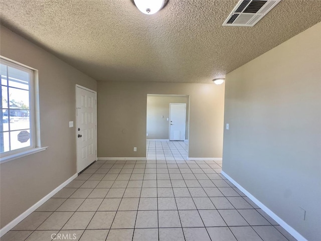 unfurnished room with light tile patterned floors, a textured ceiling, visible vents, and baseboards