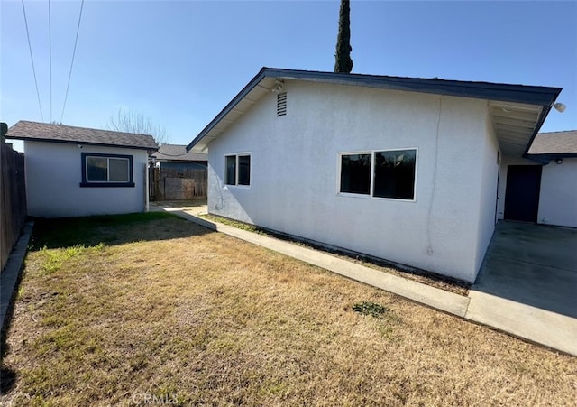 rear view of property with a lawn, fence, and stucco siding