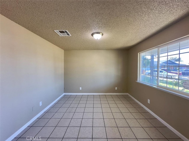 empty room featuring light tile patterned floors, a textured ceiling, visible vents, and baseboards