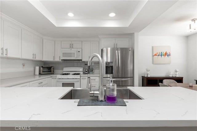 kitchen with white appliances, light stone countertops, recessed lighting, white cabinets, and tasteful backsplash