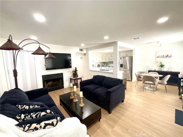 living room featuring recessed lighting, a fireplace, light wood finished floors, and visible vents