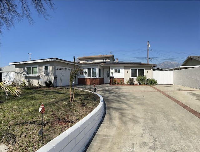 view of front of property featuring a garage, concrete driveway, fence, roof mounted solar panels, and a front lawn