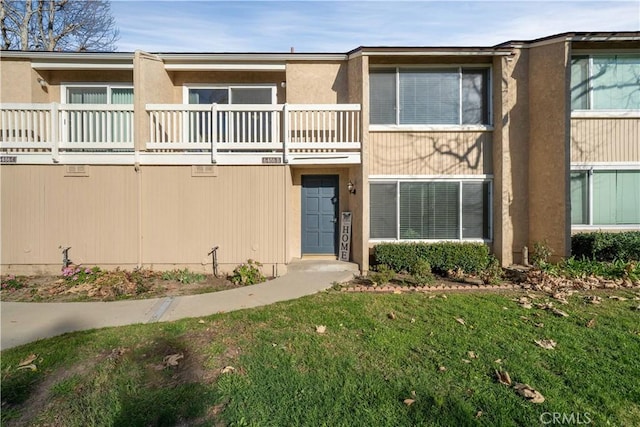 view of front of property with a balcony, a front lawn, and stucco siding