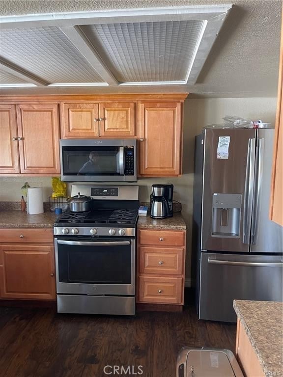 kitchen with brown cabinetry, appliances with stainless steel finishes, and dark wood finished floors