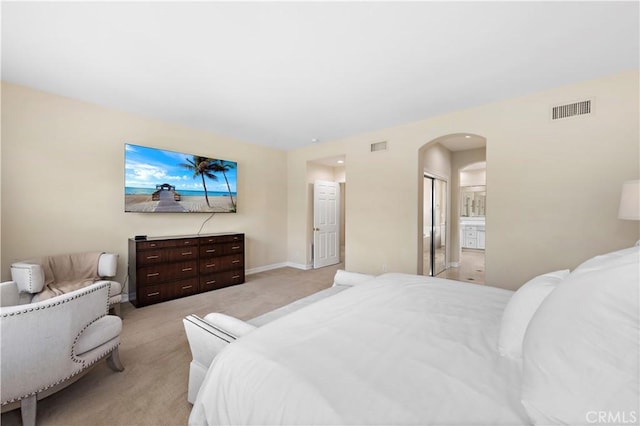 bedroom featuring arched walkways, connected bathroom, light carpet, visible vents, and baseboards