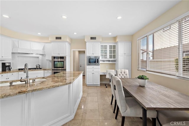 kitchen featuring light stone counters, stainless steel appliances, glass insert cabinets, white cabinets, and a sink