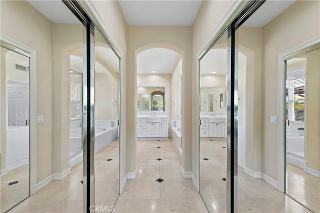 corridor with light tile patterned floors, a sink, visible vents, and baseboards