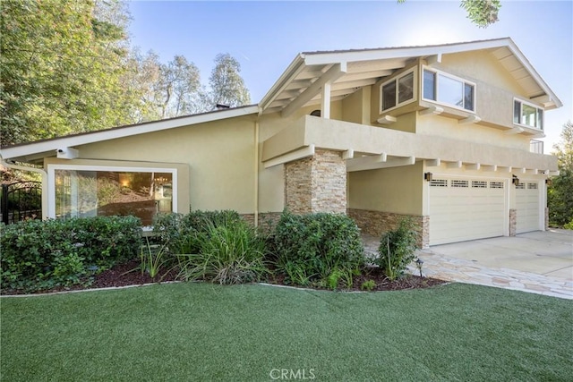 view of front of house with a garage, stone siding, concrete driveway, stucco siding, and a front lawn