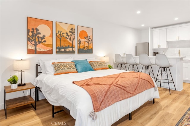 bedroom with recessed lighting, light wood-style flooring, and stainless steel refrigerator