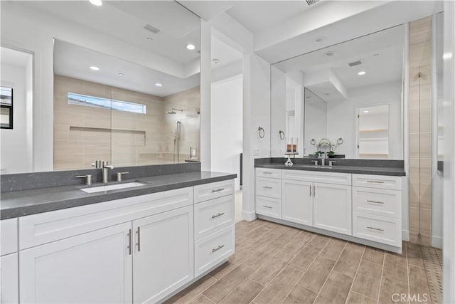 bathroom featuring a sink, wood finish floors, a walk in shower, two vanities, and recessed lighting