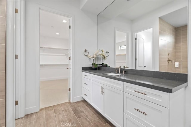 full bath with wood finish floors, a walk in closet, vanity, and baseboards