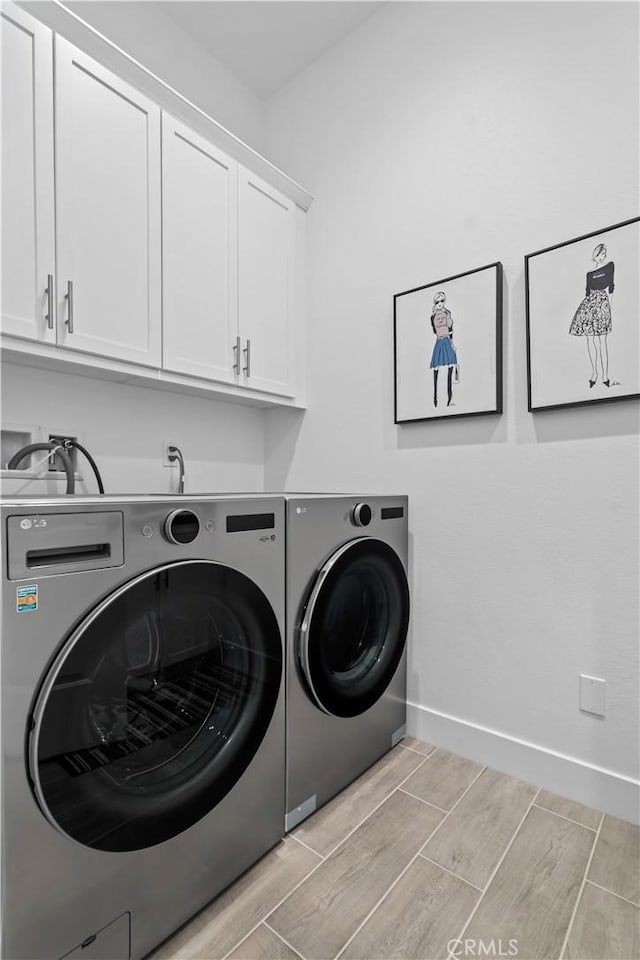 laundry area featuring wood finish floors, washing machine and clothes dryer, cabinet space, and baseboards