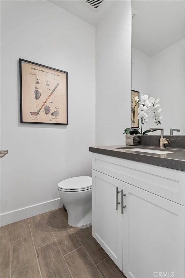 half bath with toilet, wood finish floors, vanity, and baseboards