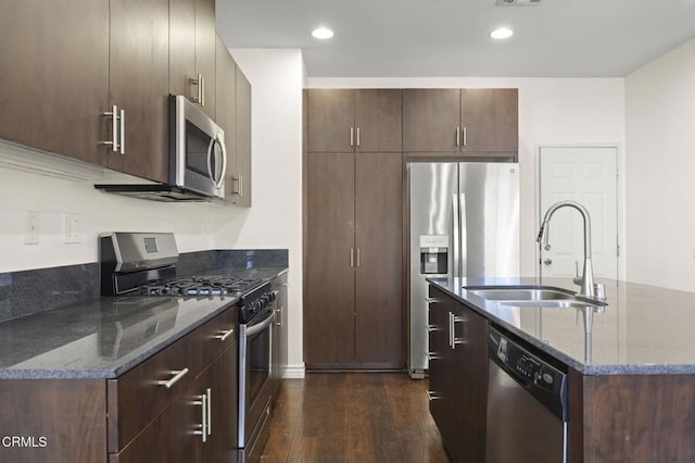 kitchen featuring dark brown cabinetry, stainless steel appliances, a sink, dark stone countertops, and dark wood finished floors