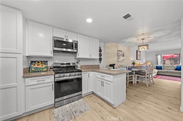 kitchen with open floor plan, a peninsula, appliances with stainless steel finishes, and white cabinetry