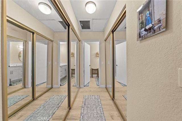 hallway featuring a textured wall, light wood-type flooring, visible vents, and baseboards