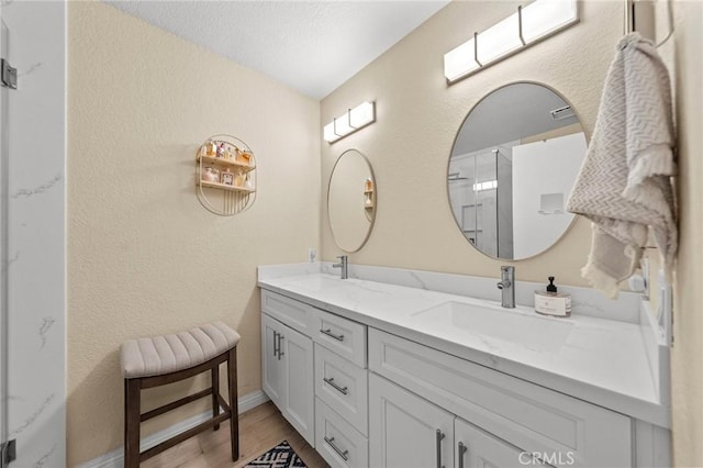 full bath with a textured wall, double vanity, wood finished floors, and a sink