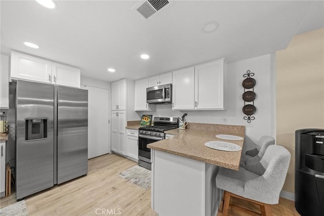 kitchen with visible vents, white cabinets, appliances with stainless steel finishes, a peninsula, and a kitchen bar