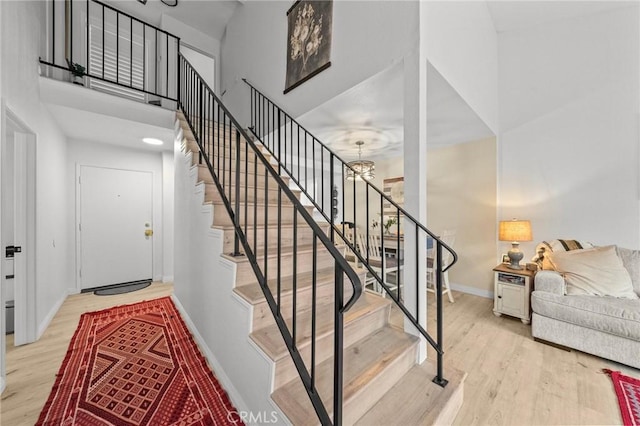 staircase with a high ceiling, baseboards, a chandelier, and wood finished floors