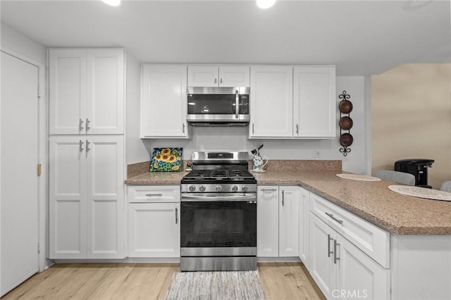 kitchen with stainless steel appliances, white cabinets, light wood-style flooring, and light stone countertops