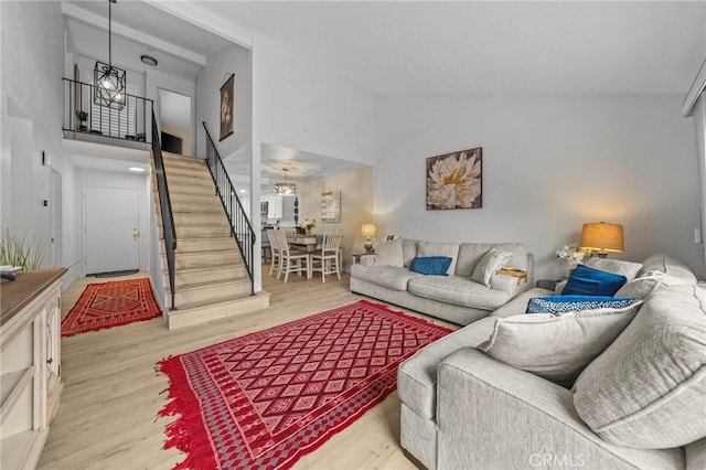 living area with high vaulted ceiling, stairway, and light wood-style flooring