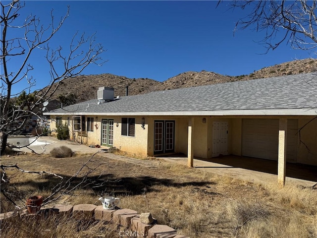 back of property featuring central AC unit, a chimney, roof with shingles, a mountain view, and stucco siding