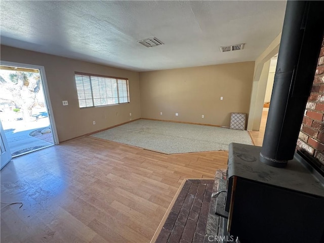 unfurnished living room with visible vents, a wood stove, and a healthy amount of sunlight