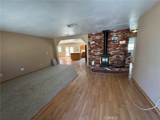 unfurnished living room featuring arched walkways, a wood stove, a textured ceiling, light wood-type flooring, and baseboards