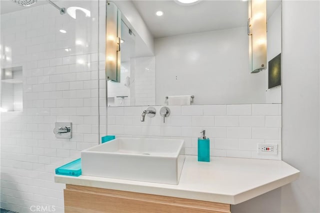 full bathroom with tiled shower, vanity, and tile walls