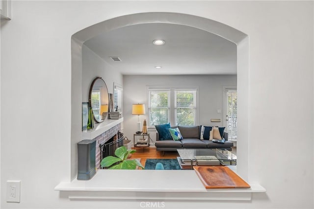 living room featuring visible vents, arched walkways, wood finished floors, a brick fireplace, and recessed lighting