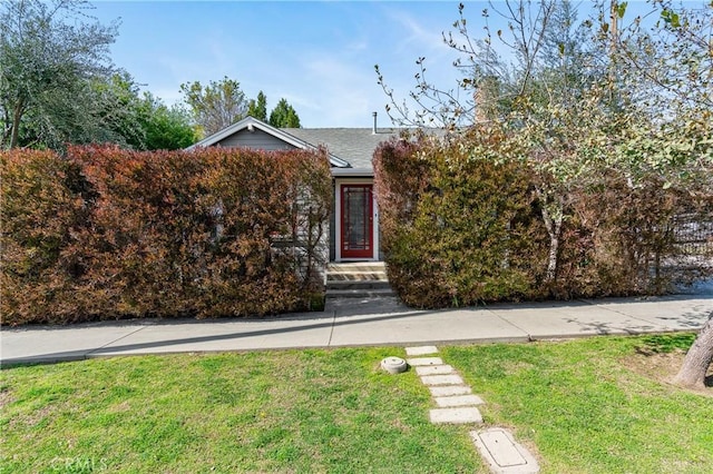 view of property hidden behind natural elements featuring a shingled roof and a front yard