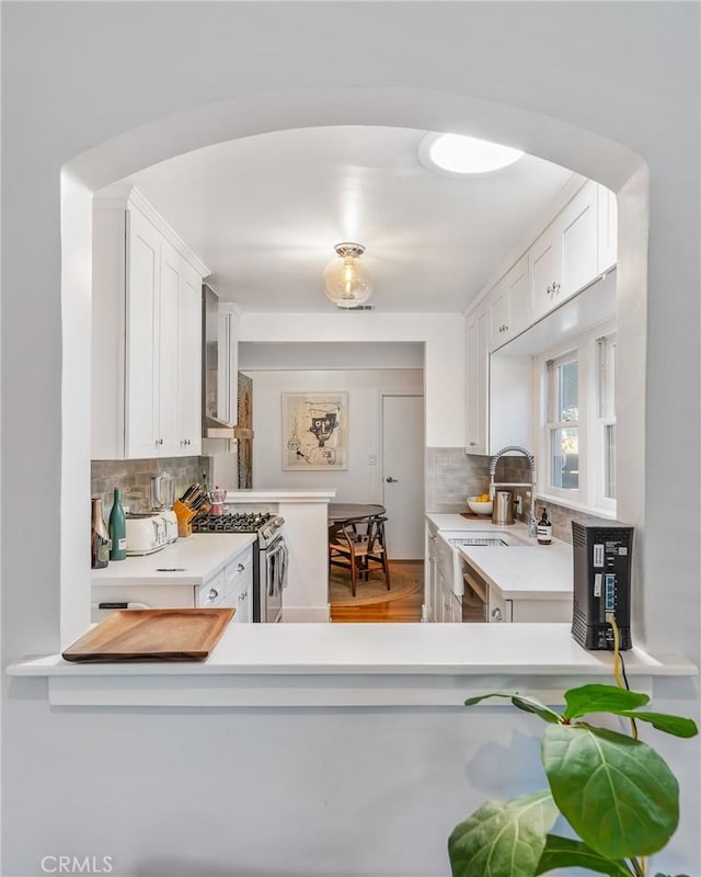 kitchen featuring arched walkways, tasteful backsplash, light countertops, white cabinetry, and stainless steel gas range oven