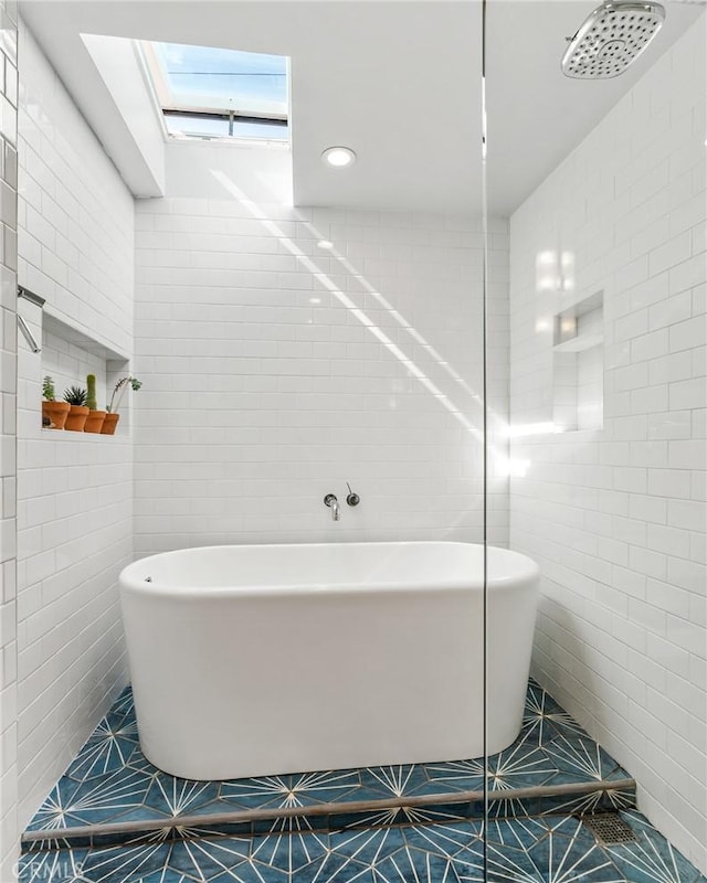 bathroom with tile patterned flooring, a skylight, tile walls, a freestanding bath, and tiled shower