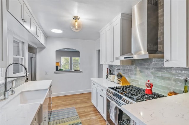 kitchen with stainless steel range with gas cooktop, white cabinetry, a sink, wall chimney range hood, and light stone countertops