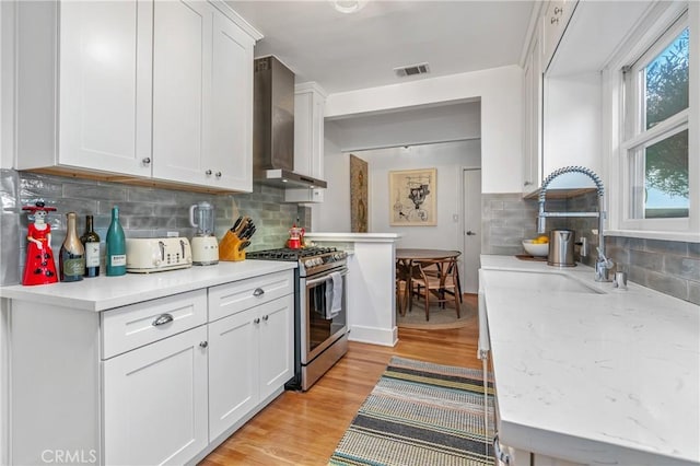 kitchen featuring visible vents, white cabinetry, wall chimney range hood, stainless steel gas stove, and light wood finished floors