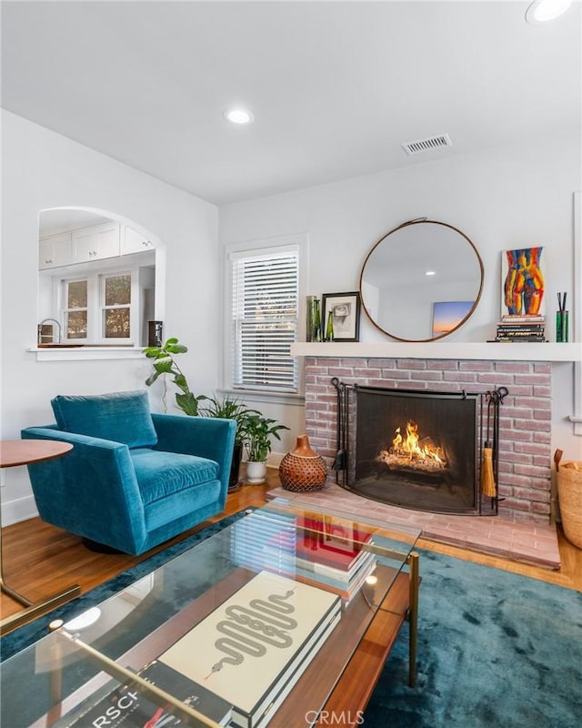 living room featuring a brick fireplace, visible vents, wood finished floors, and recessed lighting