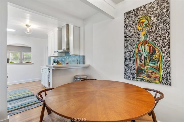 dining area with arched walkways, light wood finished floors, and baseboards