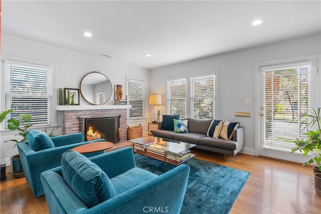 living area featuring a healthy amount of sunlight, a brick fireplace, wood finished floors, and recessed lighting