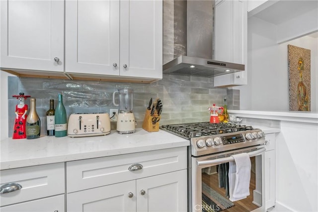 kitchen featuring stainless steel gas range, white cabinetry, wall chimney exhaust hood, and light stone countertops