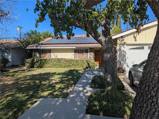 ranch-style home featuring roof mounted solar panels, an attached garage, and a front lawn