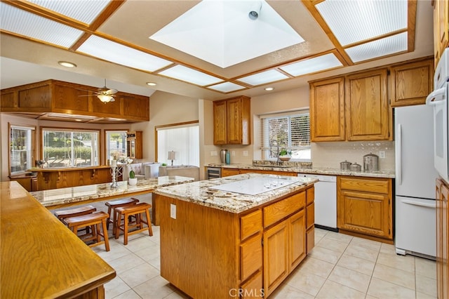 kitchen featuring a center island, tasteful backsplash, lofted ceiling, brown cabinetry, and white appliances