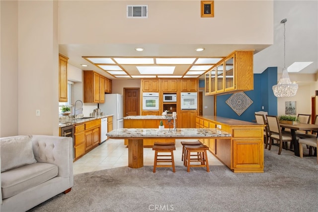 kitchen featuring a breakfast bar, light countertops, hanging light fixtures, glass insert cabinets, and white appliances