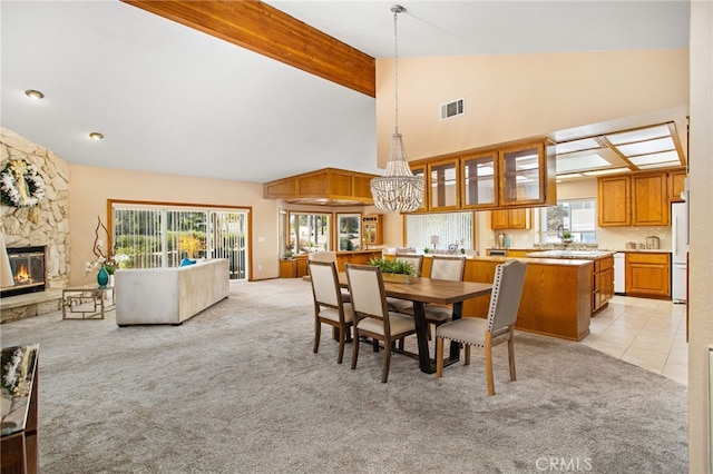 dining area featuring beamed ceiling, a fireplace, visible vents, and light colored carpet