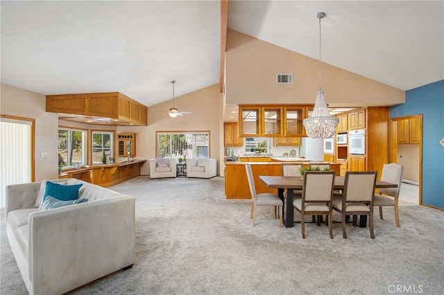 dining space featuring high vaulted ceiling, visible vents, light carpet, and ceiling fan with notable chandelier