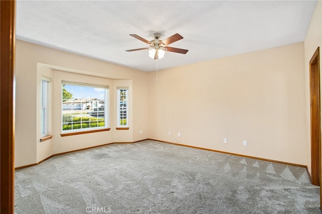 carpeted spare room featuring ceiling fan and baseboards