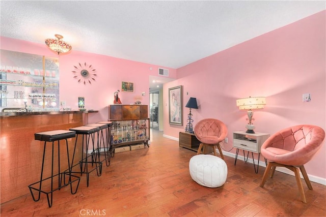 sitting room with a dry bar, wood finished floors, visible vents, and baseboards