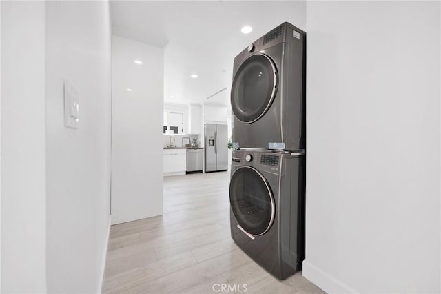 clothes washing area featuring light wood-style flooring, recessed lighting, laundry area, stacked washer / dryer, and a sink